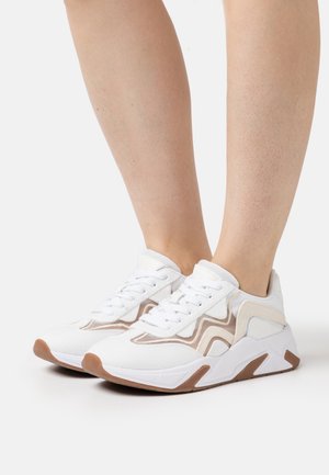 Białe sportowe trampki z beżowymi akcentami, teksturowaną tkaniną, sznurowanym fasonem i gumową podeszwą z brązowym obcasem i detalami po bokach.
