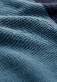 Kék árnyalataiban szőtt szövet texturált felülettel, amely vízszintes vonalakat és puha, hívogató megjelenést mutat.