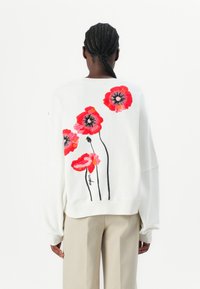 Felpa bianca con ricami colorati di fiori rossi e rosa con contorni neri sulla schiena. Vestibilità ampia con maniche drop.