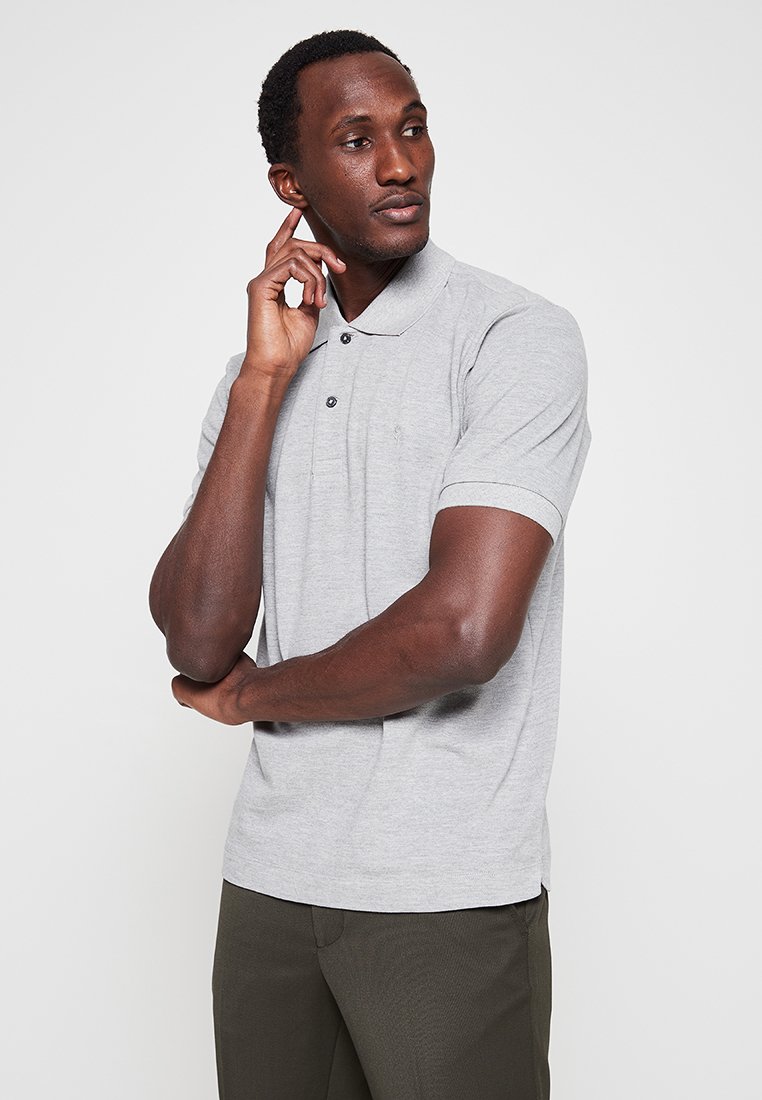 Graues Poloshirt mit kurzen Ärmeln und Kragen, zwei Knöpfen und einem dezenten Logo. Trägt man mit dunkelgrünen Hosen, die glatte Stoffoberfläche ist sichtbar.