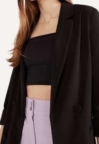 Černý blazer se dvěma velkými knoflíky, nošený přes černý krátký top, doplněný o kalhoty v levandulové barvě s vysokým pasem a dvouknoflíkovým zapínáním.