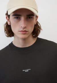 Černé tričko s kulatým výstřihem a bílým logem "Marc O'Polo DENIM" na hrudi, kombinované s bílou čepicí. Hladká bavlněná textilie.