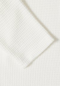 Tissu blanc en maille gaufrée plié pour montrer le motif texturé et l'épaisseur, avec un éclairage doux mettant en valeur les détails du matériau.