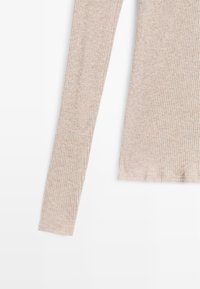 Top a maniche lunghe a coste color beige chiaro, caratterizzato da una finissima texture e da una forma aderente con scollatura rotonda.
