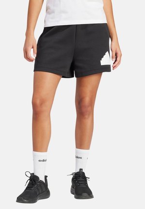 Pantalones cortos deportivos negros hechos de una mezcla de algodón, con un acento de logo blanco y un ajuste relajado. Se llevan con zapatos negros y calcetines blancos.
