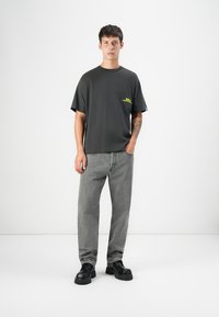 Gray oversized t-shirt with a neon green logo, paired with gray jeans and black chunky shoes, standing against a plain white background.