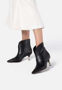Bottes chelsea noires en cuir avec des bouts pointus et des poignets incurvés, présentant un talon conique en métal argenté et une texture lisse.