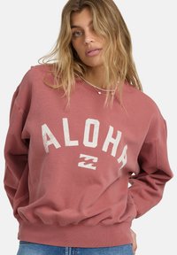 Ružová mikina s nápisom "ALOH" v bielej farbe, voľný strih, rebrované manžety a lem, vyrobená z mäkkej textúrovanej látky.
