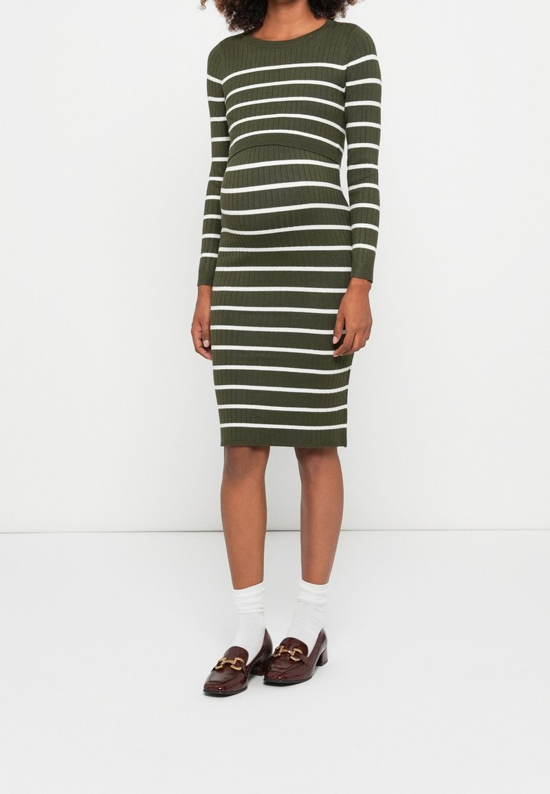 Femme portant une robe moulante côtelée vert olive avec des rayures blanches horizontales, des chaussettes blanches et des mocassins marron avec des ornements dorés.