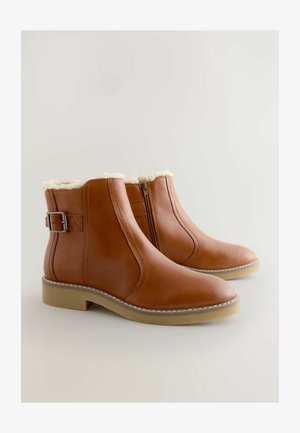 Bruine leren enkelboots met zijrits, gespdetail, faux bont voering en lichte rubberen zolen op een neutrale achtergrond.