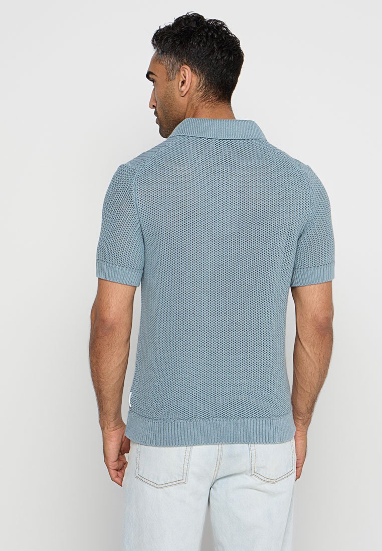 Hellblaues Kurzarm-Polohemd mit strukturiertem Strickdesign, geripptem Kragen und Saum, versehen mit einem kleinen Seitenlabel.