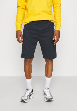 Marineblauwe cargoshorts met zijzakken, gemaakt van katoen, met een recht model en omgeslagen zoom, gecombineerd met een geel sweatshirt en sneakers.