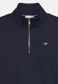 Sudadera de media cremallera en azul marino hecha de una mezcla de algodón. Presenta una cremallera plateada y un pequeño logotipo bordado. Textura suave, diseño casual.