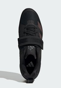 Czarne buty sportowe z teksturowaną cholewką, sznurowaniem i regulowanym paskiem. Wyraźne logo Adidas w pobliżu pięty.