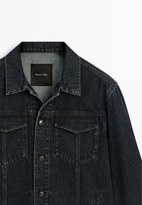 Dunkelblaue Jeansjacke mit vorderen Klappentaschen, Metallknöpfen und einem Kragen, innen im Nacken mit "Massimo Dutti" beschriftet.