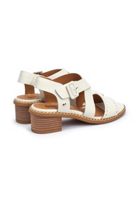 White leather sandals with a cross-strap design, featuring a buckle, a textured light brown block heel, and visible stitching details.