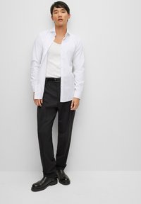 Camisa blanca de botones, de mangas largas, corte ajustado; combinada con pantalones negros y botas negras. Tela lisa y sólida sin patrones visibles.