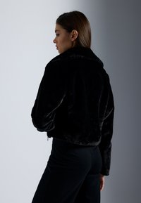 Zwarte nepbont korte jas met kraag, voorzien van lange mouwen, een rits en een zachte textuur. Gestyled met zwarte broek.