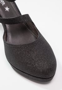 Chaussure Mary Jane noire pailletée à bout fermé avec une bride unique sur le cou-de-pied et des coutures visibles le long de la semelle intérieure.