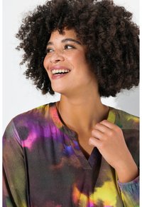 Blusa colorida de tie-dye con escote en V y mangas largas. La tela parece suave con una mezcla de tonos púrpura, amarillo y verde.
