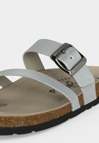 Λευκό δερμάτινο σανδάλι με δύο λουριά, το ένα με μια μεγάλη ασημένια αγκράφα, πάτος από φελλό και μαύρη καουτσούκ σόλα.