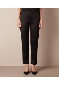 Svarta satinbyxor med elastisk midja, avsmalnande design och slät textur. Funktionerna är minimalistiska utan fickor eller utsmyckningar.