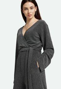 Vestido envolvente gris con mangas largas, escote en pico y cinturón anudado en la cintura. Fabricado con una tela texturizada con un leve brillo.