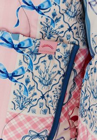 Prošité látky s květinovým a kostkovaným vzorem v modré a růžové barvě. Obsahuje mašle a růžovou etiketu s grafikou slunce.
