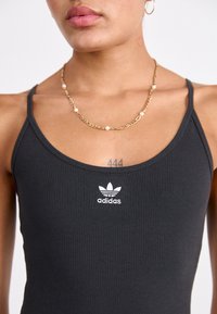 Černý žebrovaný top bez rukávů s tenkými ramínky a bílým logem Adidas na hrudi, doplněný zlatým náhrdelníkem s perlami.