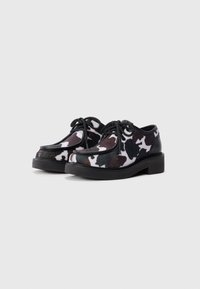 Chaussures imprimées vache en matériau doux, avec un bout arrondi, des lacets noirs et une semelle plateforme noire robuste. Motif de couleur distinctif.
