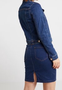 Mörkblå denimjacka med en figurnära design, knappstängning och kort längd, i kombination med en matchande kjol med en bakre slits.
