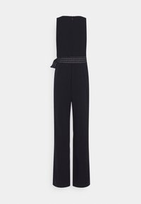 Mustaton, leveälahkeinen jumpsuit ilman olkaimia, jossa on musta-valkoinen ruudullinen vyö solmittuna vyötärölle.