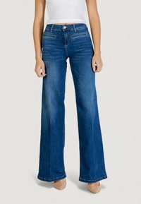 Tummansiniset leveälahkeiset farkut, joissa etutaskut ja nappikiinnitys. Sileä pinta ja suora helma alareunassa.