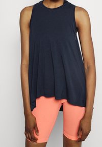 Débardeur bleu marine avec un design évasé et un col rond, associé à un short corail ajusté. Le tissu semble doux et lisse.