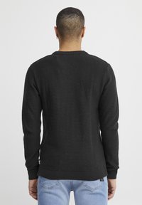 Zwart textuurtrui met lange mouwen, ronde hals en een geribbelde zoom. Gedragen over lichtblauwe jeans, wat een casual stijl laat zien.