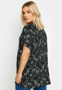 Blusa nera a fiori con maniche corte e vestibilità comoda, caratterizzata da motivi floreali bianchi e una texture morbida. Il retro è più lungo del davanti.