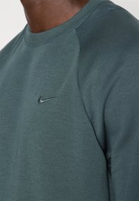Sudadera de color verde oscuro hecha de un tejido suave, con cuello redondo y mangas raglán, adornada con un pequeño logo negro de Nike en el pecho.