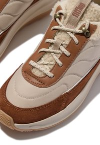 Des baskets en toile beige et en daim marron, avec une doublure moelleuse, des lacets marron et des accents décoratifs sur les côtés.
