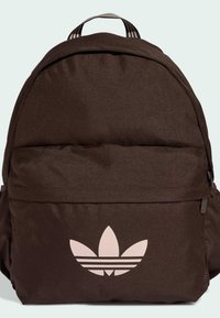 Brązowy plecak wykonany z teksturowanej tkaniny, z dużą przednią kieszenią i wyraźnym jasnoróżowym logo z trzema paskami. Regulowany uchwyt na górze.