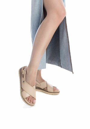 Sandalias de tiras cruzadas beige con una superficie texturizada, detalle de hebilla y suela plana estriada, combinadas con una falda de mezclilla azul.