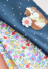 Trei mostre de materiale: o mostră albastră cu buline albe și un design cusut cu un porcușor de Guineea, și două imprimeuri florale cu flori colorate pe un fundal deschis.