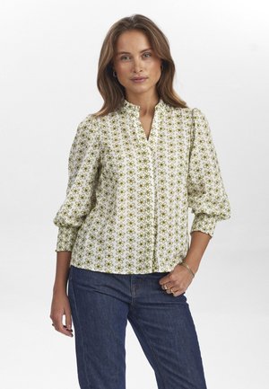 Witte blouse met groen bloemenpatroon, mandarin kraag en pofmouwen. Gecombineerd met donkerblauwe jeans. Glad stoftextuur.