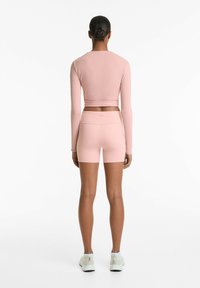 Jasnoróżowy, długi rękaw crop top zestawiony z pasującymi, wysokimi szortami. Materiał wydaje się miękki o gładkiej powierzchni.