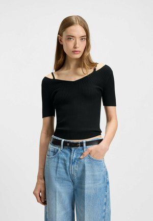 Svart ribbad stickad topp med korta ärmar, v-ringning och axelband, kombinerad med ljusblå vida jeans och ett svart bälte.