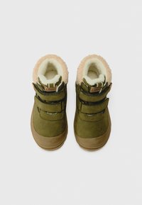 Grüne Wildlederstiefel mit beige Akzenten, doppelten Klettverschlüssen und einem flauschigen cremefarbenen Futter. Rund gestaltete Zehenpartie, geeignet für den Außenbereich.
