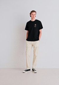 Sort bomulds t-shirt med solgrafik, parret med beige bukser og sort-hvide sneakers. Enkel, afslappet design og løs pasform.