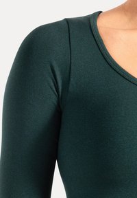 Donkergroen nauwsluitend topje met een gladde textuur en een brede V-hals. De stof lijkt licht glanzend, wat het strakke ontwerp van het kledingstuk benadrukt.