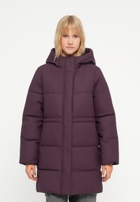 Lilla polstret ytterjakke med hette, med en quiltet design og boksform. Stoffet ser glatt ut, noe som fremhever et varmt og isolert utseende.