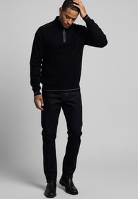Suéter negro acanalado con detalle de cuello con cremallera, combinado con jeans ajustados de mezclilla oscura y botines negros. Tela suave y cómoda.