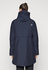 Αδιάβροχο μπουφάν σε ναυτικό μπλε χρώμα με κουκούλα, διαθέτει κρυφό κούμπωμα με κουμπί και λογότυπο στο πάνω μέρος της πλάτης. Μήκος μέχρι το μέσο του μηρού με λεία υφή.